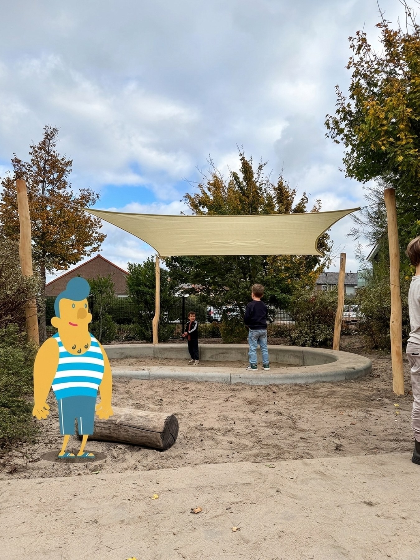 Zandkleurig Sundo schaduwdoek boven een zandbak, met de Sundude-mascotte